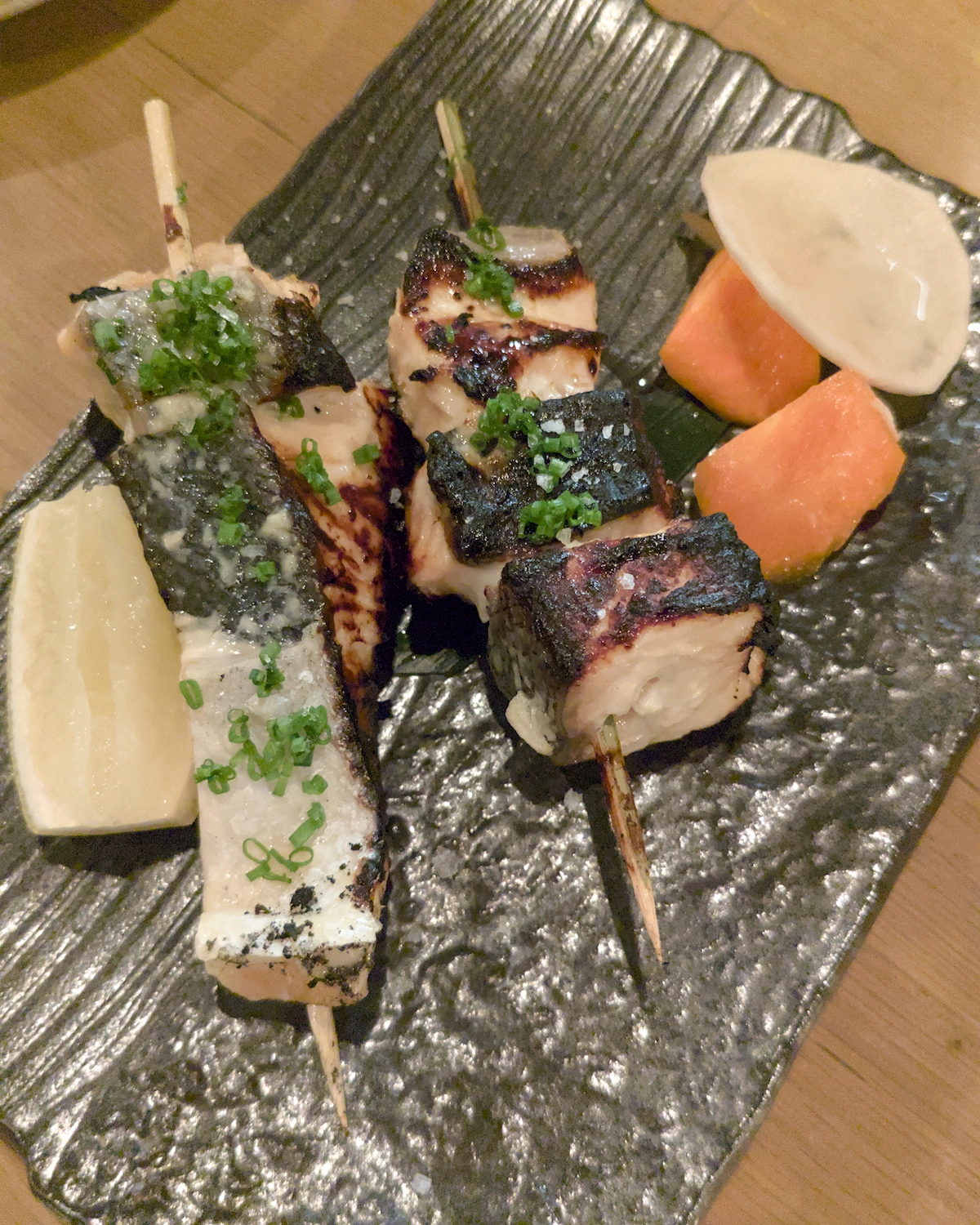 Two skewers of salmon on a grey plate with pickles