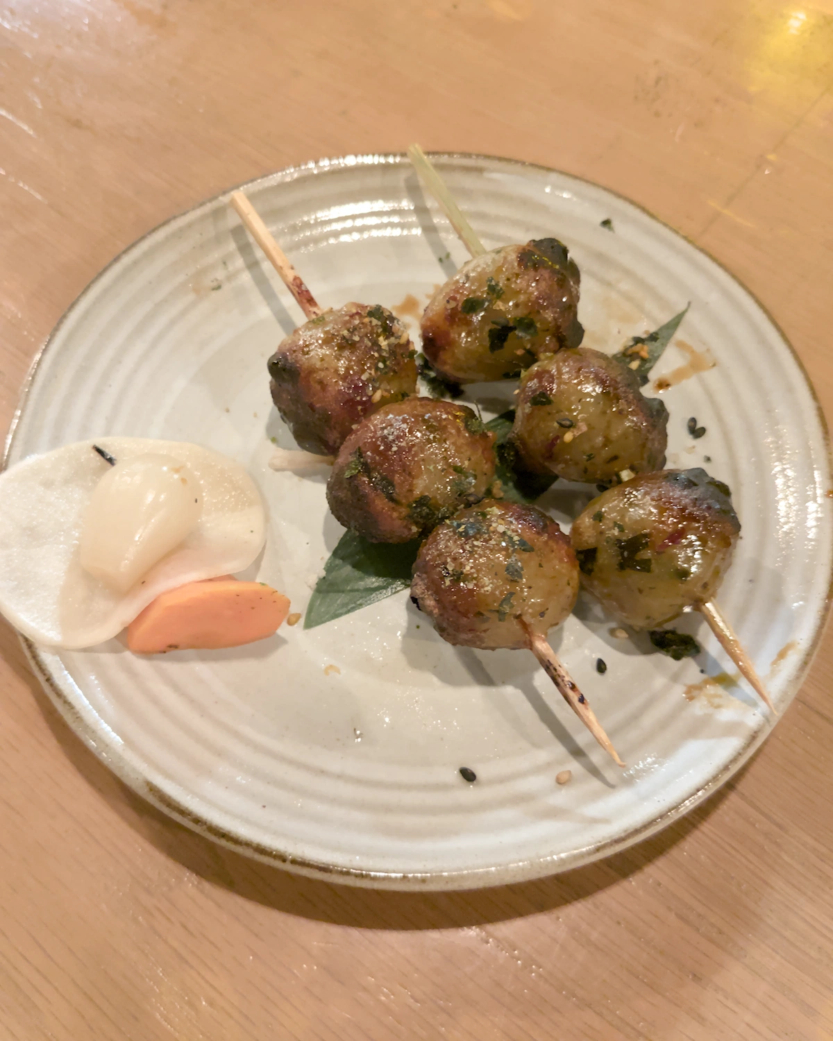 Two skewers of sweet potato mochi balls and some pickles on a white round plate
