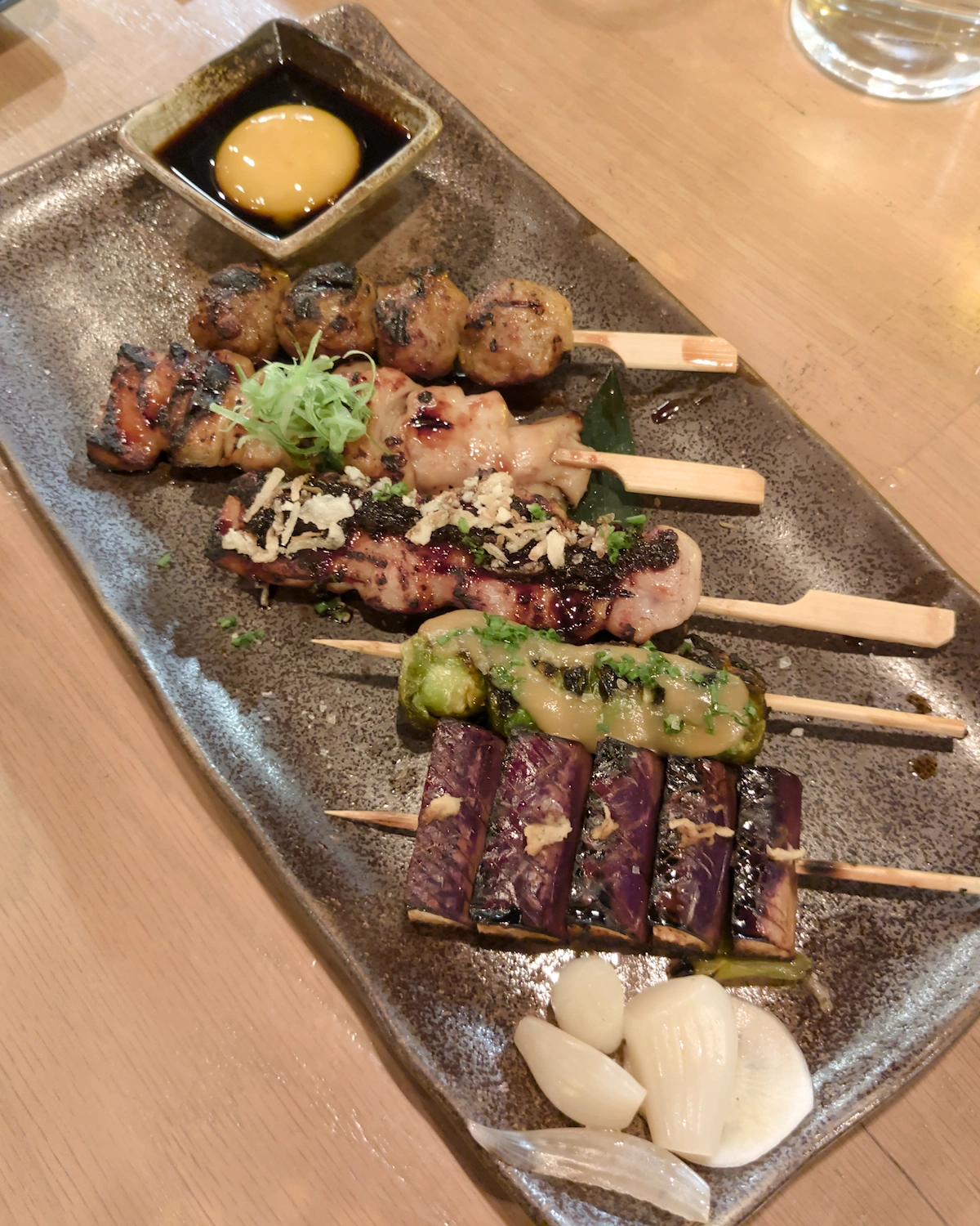 Assorted meat and vegetable skewers on a grey plate with a raw egg yolk in the background