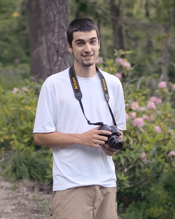 A man smiling and holding a nikon DSLR camera