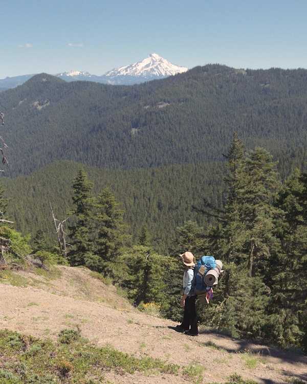 A women wearing a backpack standing on a trail looking towards a snowcapped mountain